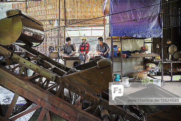 Robert Hahn (Mitte) plaudert mit vietnamesischen Arbeitern  während er ein vietnamesisches Bier trinkt  auf einer mechanischen Goldbaggeranlage  die auf dem Nam Ou Fluss in Laos schwimmt. Sechs Männer leben monatelang auf dem Schiff  wechseln sich den ganzen Tag ab und arbeiten paarweise  um die Maschine in Betrieb zu halten.