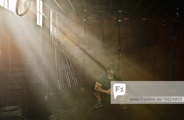 Eine Person  die Crossfit in einem alten Lagerhaus-Fitnessstudio macht  in dem Lichtstrahlen durch die Fenster eindringen.