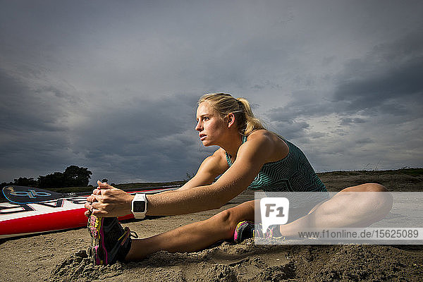 An athletic girl stretches on the beach before paddle boarding in San Diego  CA.