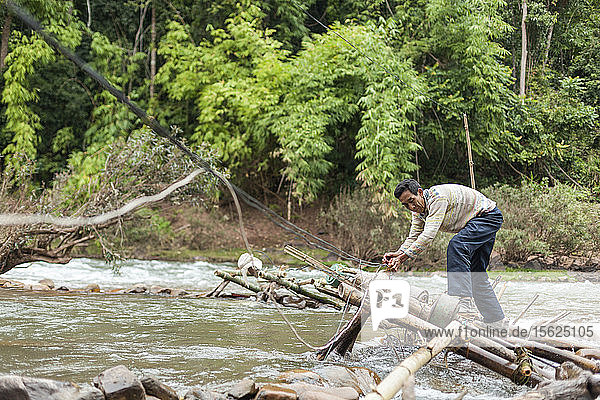 Ein Mann justiert die Mikro-Wasserturbinen im Fluss Nam Ou in Ban Sop Kha  Laos. Die Turbinen werden von den Dörfern entlang des Flusses zur Stromerzeugung genutzt  zumindest in der Trockenzeit  wenn der Wasserstand niedrig genug ist  um sie am Flussbett zu befestigen.