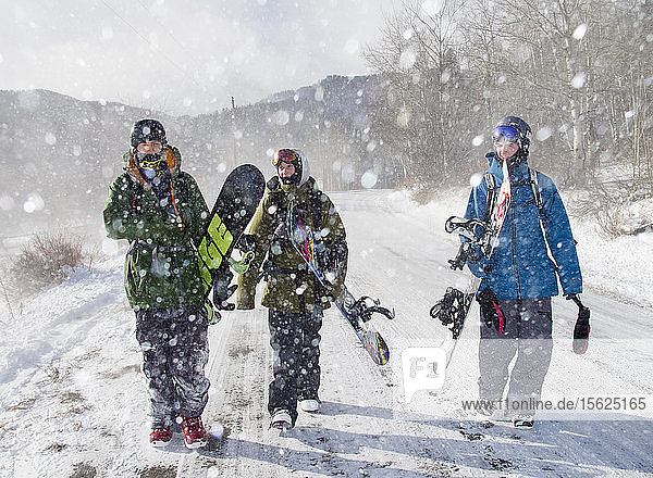 Drei Snowboarder gehen nach einer Fahrt über den Teton Pass eine verschneite Straße hinunter