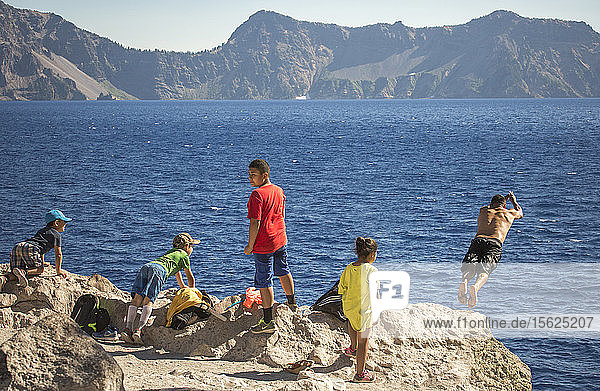 Junge Leute warten auf einem Felsvorsprung und schwimmen oder springen in das tiefblaue Wasser des Crater Lake  Oregon  USA