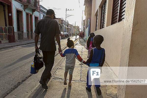 Vater  Sohn und Tochter gehen zusammen auf dem Bürgersteig und halten sich an den Händen  Santiago de Cuba  Kuba
