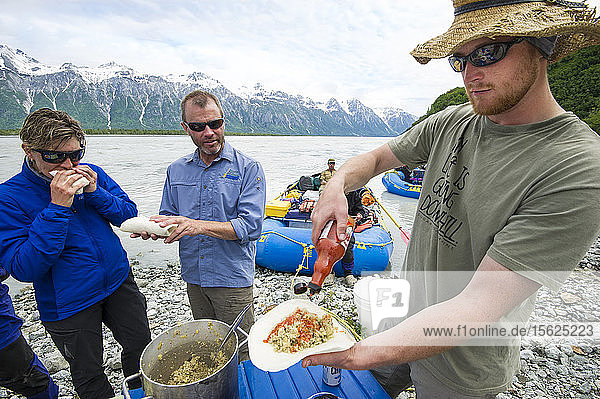 Gruppe von Flößern  die während des Mittagessens am Ufer des Alsek-Flusses Hotsauce genießen