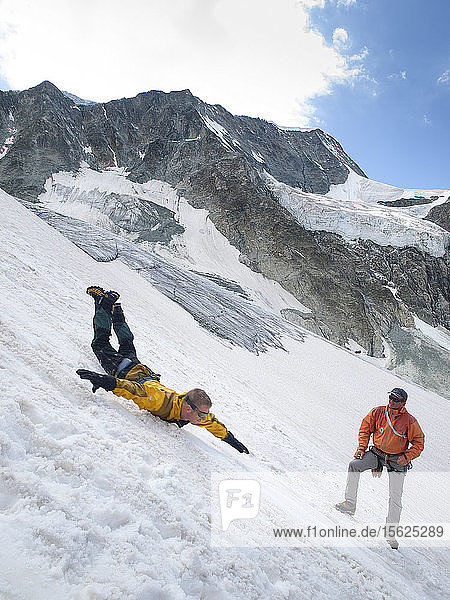Bei einem Sicherheitstraining für Bergsteiger rutscht ein Schüler einen steilen Gletscherhang hinunter und versucht  sich abzusichern  während der Lehrer  ein Bergführer  Ratschläge gibt  Moiry-Gletscher  Wallis  Schweiz