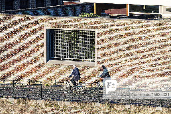 Photograph with side view of senior man riding bicycle past buildings in Wyck-Ceramique quarter  Maastricht  Limburg  Netherlands