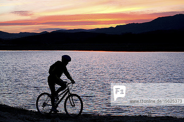Silhouette of man mountain biking in San Juan reservoir during sunset