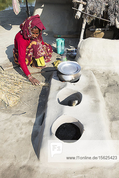 Eine Subsistenzbäuerin kocht auf einem traditionellen Lehmofen und verwendet Reisstängel als Biobrennstoff in den Sundarbans im Ganges-Delta in Indien. Das Gebiet liegt sehr niedrig und ist durch den Anstieg des Meeresspiegels gefährdet. Alle Teile der Reisernte werden verwendet  und die Dorfbewohner leben sehr autark  mit einem winzigen Kohlenstoff-Fußabdruck.