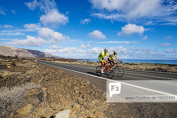 Zwei Rennradfahrer fahren nebeneinander auf einer Straße in Küstennähe  Lanzarote  Kanarische Inseln  Spanien