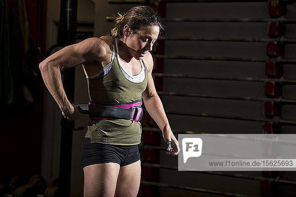A female crossfit athlete tightens her weight belt before working out at a gym in San Diego  California.