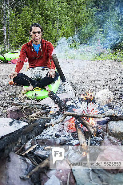 Ein Mann  der eine mehrtägige Kajaktour auf dem Middle Fork des Flathead River unternimmt  sitzt am Lagerfeuer.