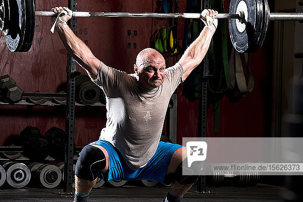 An athletic male works out with heavy weight on a barbell at a gritty gym in San Diego  California.