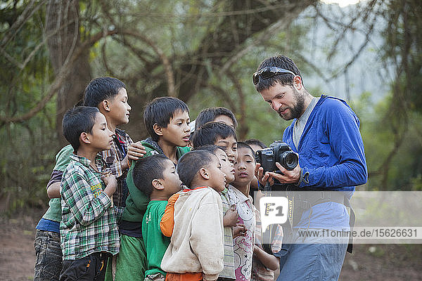 Robert Hahn shows pictures from the back of his digital camera to a group of curious boys gathered on the beach in Muang Hat Hin  Laos.