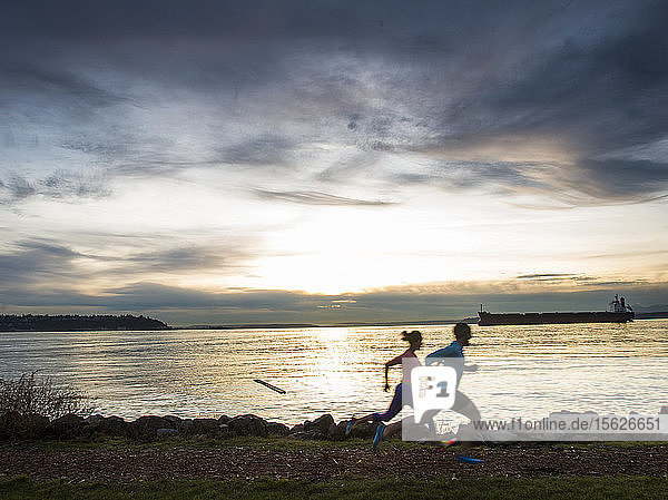 Seitenansicht eines Mannes und einer Frau  die bei Sonnenuntergang am Puget Sound entlanglaufen  Seattle  Washington State  USA