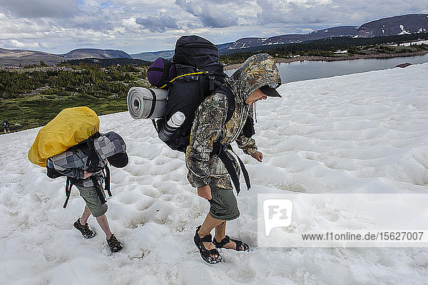 Boys endure cold feet as they carry their heavy packs across a snowfield while wearing sandals  above Superior Lake on the third day of Troop 693's six day backpack trip through the High Uintas Wilderness Area  Uintas Range  Utah