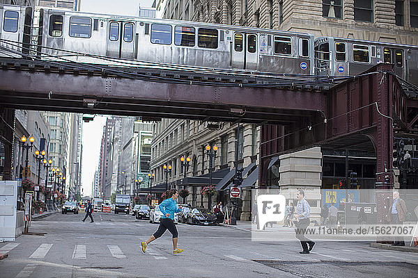 Eine erwachsene Frau  die durch die Straßen der Innenstadt von Chicago läuft  mit einer Hochbahn im oberen Teil des Bildes.