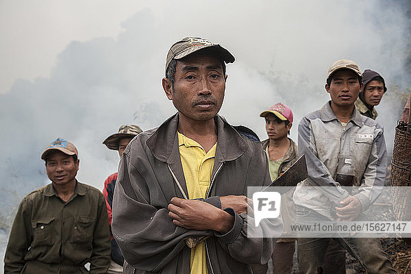 Men stand in wait with machetes as brush fires burn on the hillside above Muang Va  Laos where villagers are temporarily relocating their homes. The existing town will be completely inundated by Nam Ou River Dam #6 and the government provided resettlement near Hat Sa will not be completed in time.