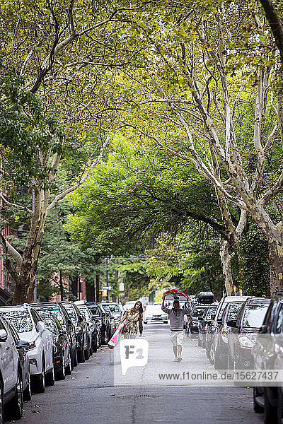 Paar mit Paddelbrettern in der Mitte der Straße zwischen Reihen geparkter Autos  New York City  New York  USA