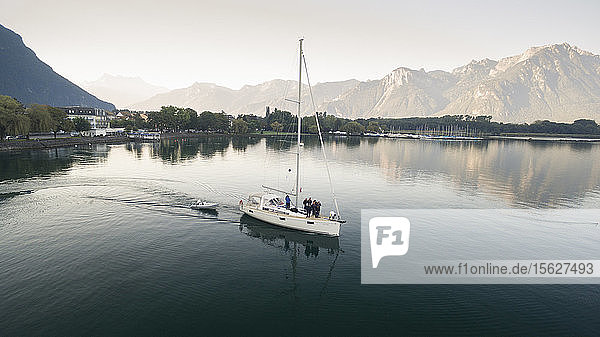 aerial view on a sailing boat and rescue boat crossing the Geneva Lake  with mountains in the background  trees on the lake's banks and a marina in Villeneuve  Vaud Canton  Switzerland
