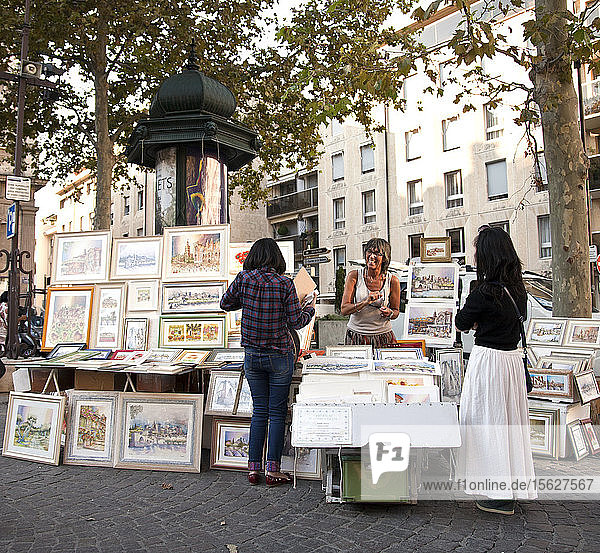 Die Künstlerin Pascale Cozic begrüßt zwei Touristen an ihrem Kunststand auf der Place de L'Horloge in Avignon  Frankreich.