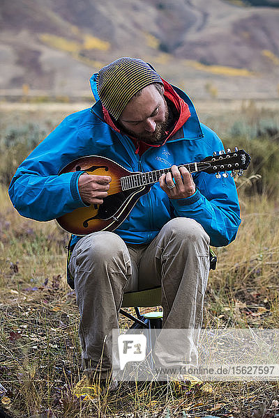 Männlicher Camper in Jacke und Strickmütze  der sitzend Mandoline spielt  Jackson  Wyoming  USA
