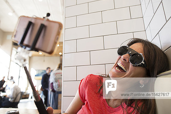 Lachende Frau  die in einem Café ein Selfie mit einem Selfie-Stick macht  Santa Cruz  Kalifornien  USA