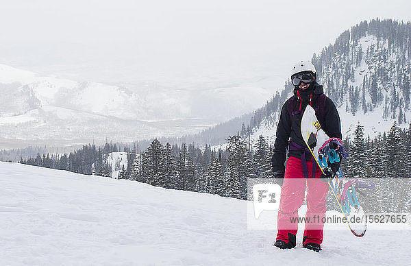 A girl stands and takes a quick break after hiking with her snowboard in the Utah Backcountry.