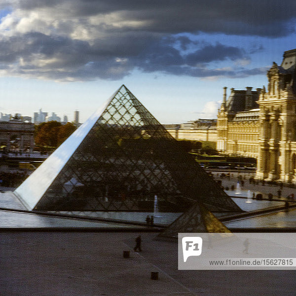 Blick durch eine Fensterscheibe auf das Musée du Louvre und die gläserne Pyramide bei stürmischem Himmel. Paris  Frankreich. Weichzeichner.