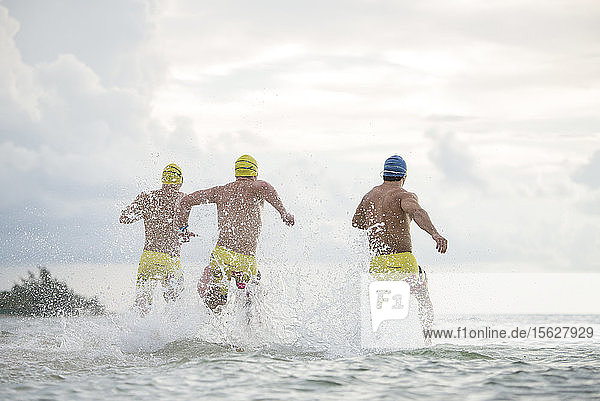 Rückansicht von drei Männern mit Badekappen und Badehosen  die in Playa del Carmen  Quintana Roo  Mexiko  ins Meer laufen