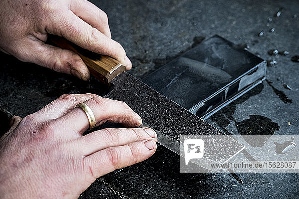 High angle close up of person sharpening handmade knife on a whetstone.