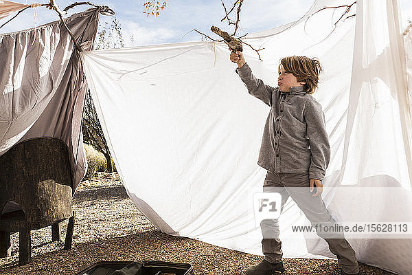 Sechsjähriger Junge spielt in einem Außenzelt aus Laken
