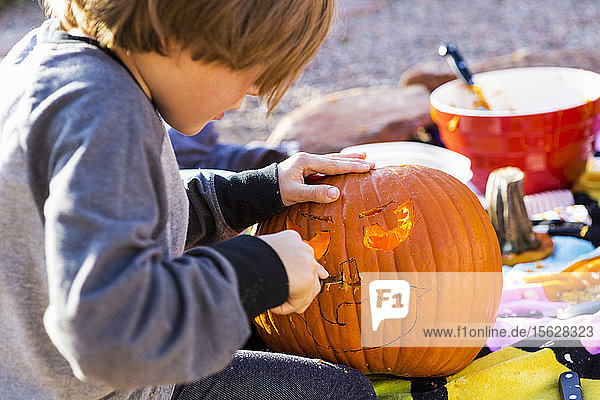 Ein sechsjähriger Junge schnitzt an Halloween einen Kürbis im Freien.