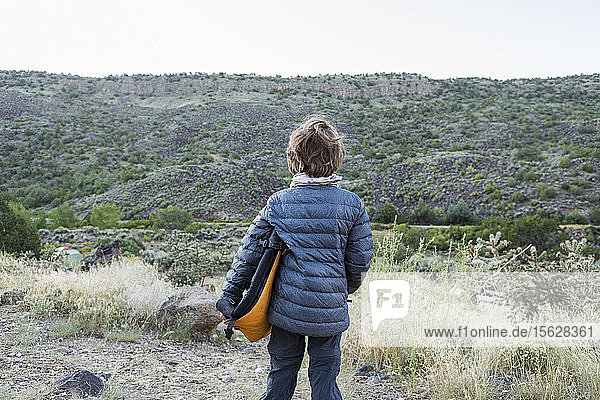 rear view of Six year old boy holding folded camp chair looking at canyon wall