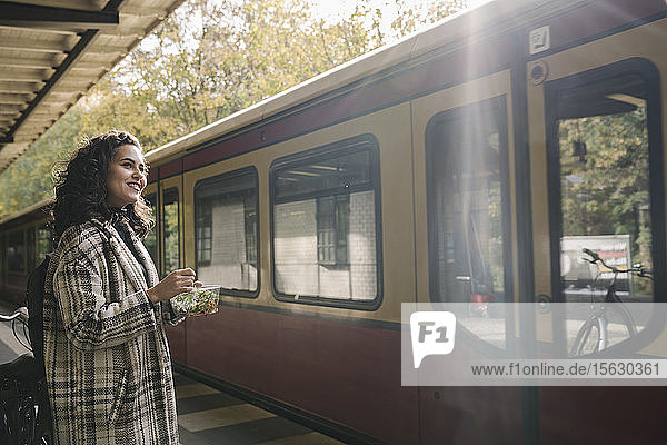 Lächelnde Frau beim Mittagessen auf einem U-Bahn-Bahnsteig  Berlin  Deutschland