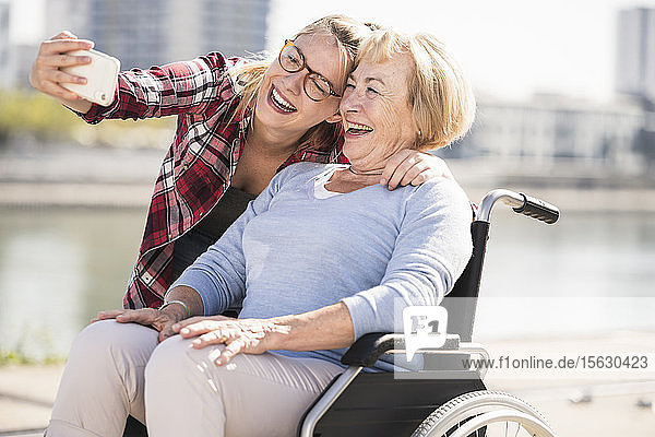 Young woman with her smiling grandmother sitting in wheelchair and taking a selfie