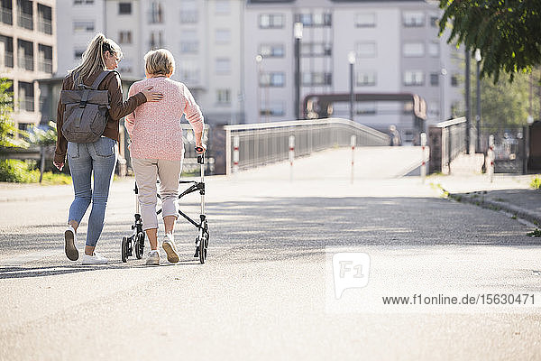 Enkelin hilft ihrer Großmutter beim Laufen mit einer Gehhilfe auf Rädern