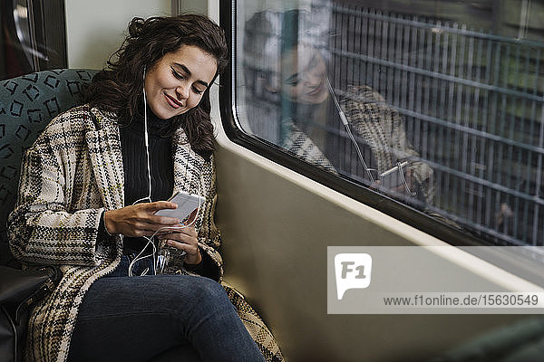 Young woman with earphones using smartphone on a subway