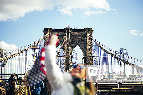 Frau steht auf der Brooklyn Bridge und hält die amerikanische Flagge  New York  Vereinigte Staaten