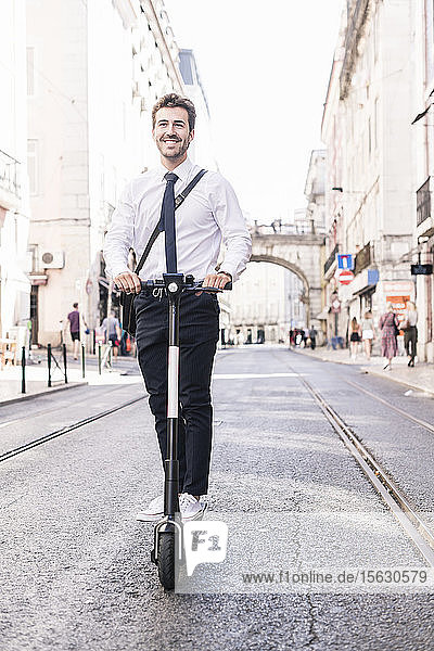 Glücklicher junger Geschäftsmann auf dem E-Scooter in der Stadt  Lissabon  Portugal