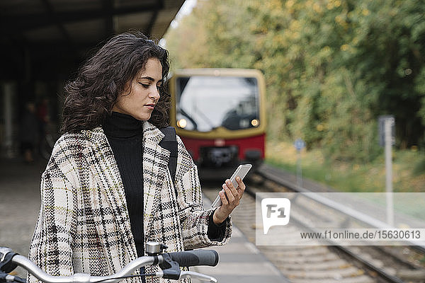 Frau mit Fahrrad und Handy auf einem U-Bahn-Bahnsteig  Berlin  Deutschland