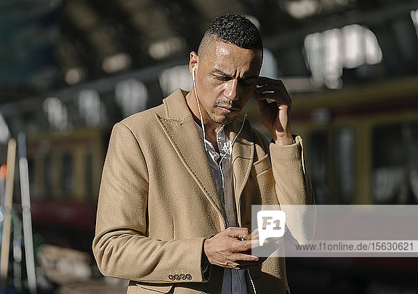 Businessman at train station Alexanderplatz using earbuds and smartphone  Berlin  Germany