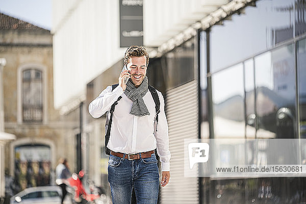 Lächelnder junger Mann mit Rucksack am Telefon in der Stadt