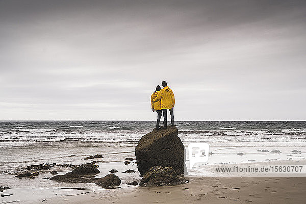 Junge Frau in gelben Regenjacken und auf einem Felsen am Strand stehend  Bretagne  Frankreich