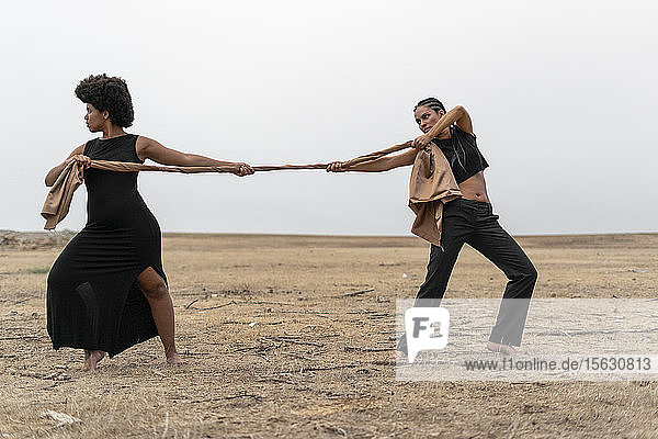 Two women pulling a cloth in bleak landscape