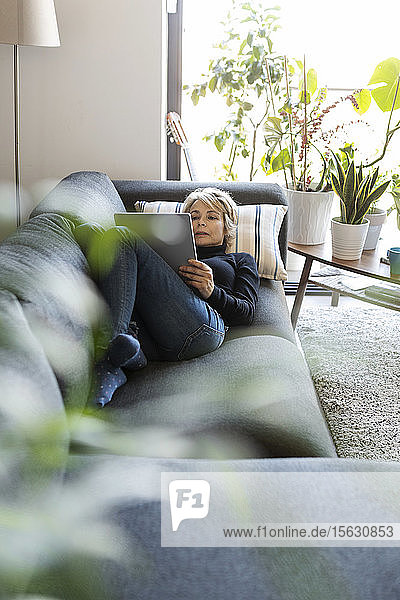 Reife Frau entspannt sich zu Hause auf der Couch mit Tablette
