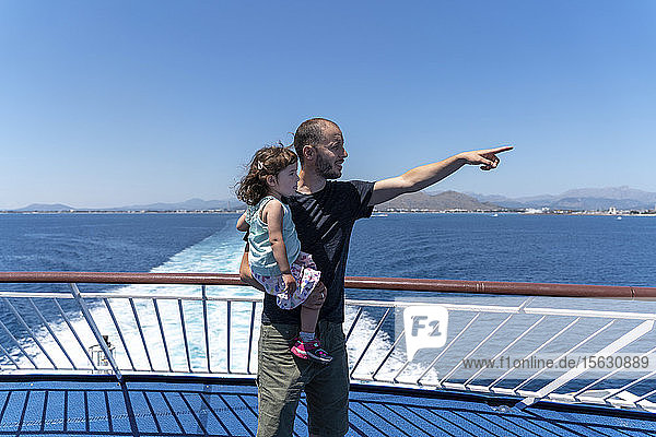 Vater steht auf dem Deck eines Schiffes mit einer kleinen Tochter auf dem Arm  die in die Ferne zeigt  Mallorca  Spanien
