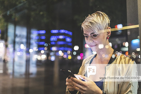 Portrait of smiling blond woman using mobile phone in the city at night  Berlin  Germany