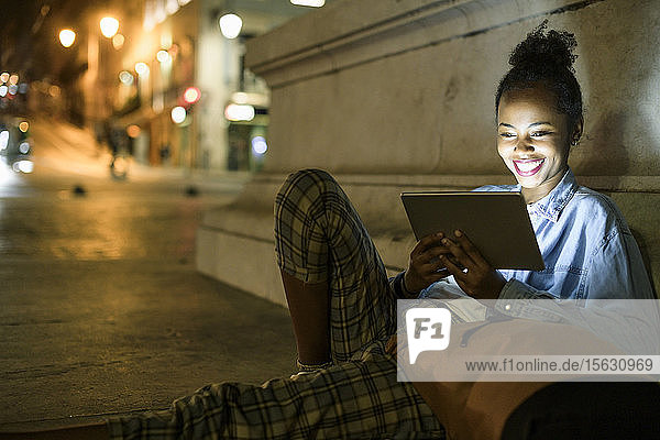 Portrait of happy young woman using digital tablet in the city by night  Lisbon  Portugal