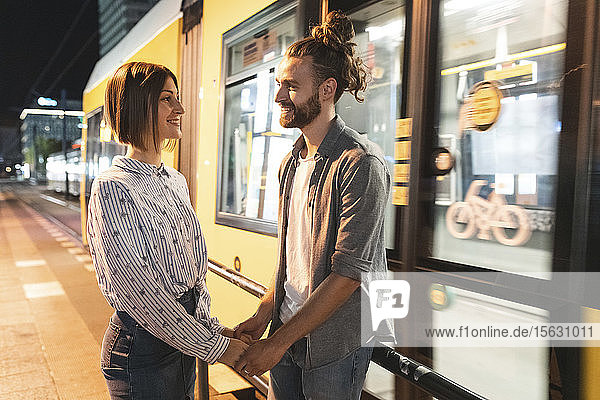 Lächelndes Paar  das sich an den Händen hält und sich mit der Straßenbahn im Hintergrund anschaut  Berlin  Deutschland