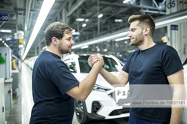 Zwei Kollegen schütteln sich in moderner Autofabrik die Hand